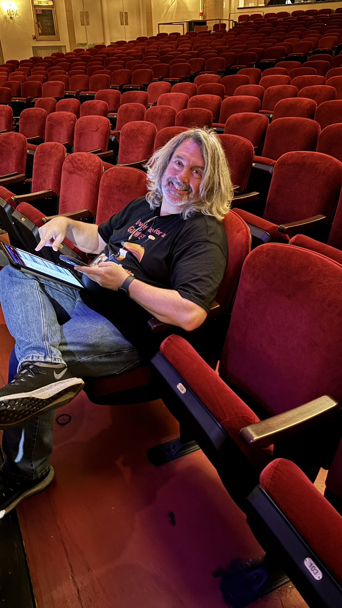 Paul O'Dell sitting in an empty theater with a tablet