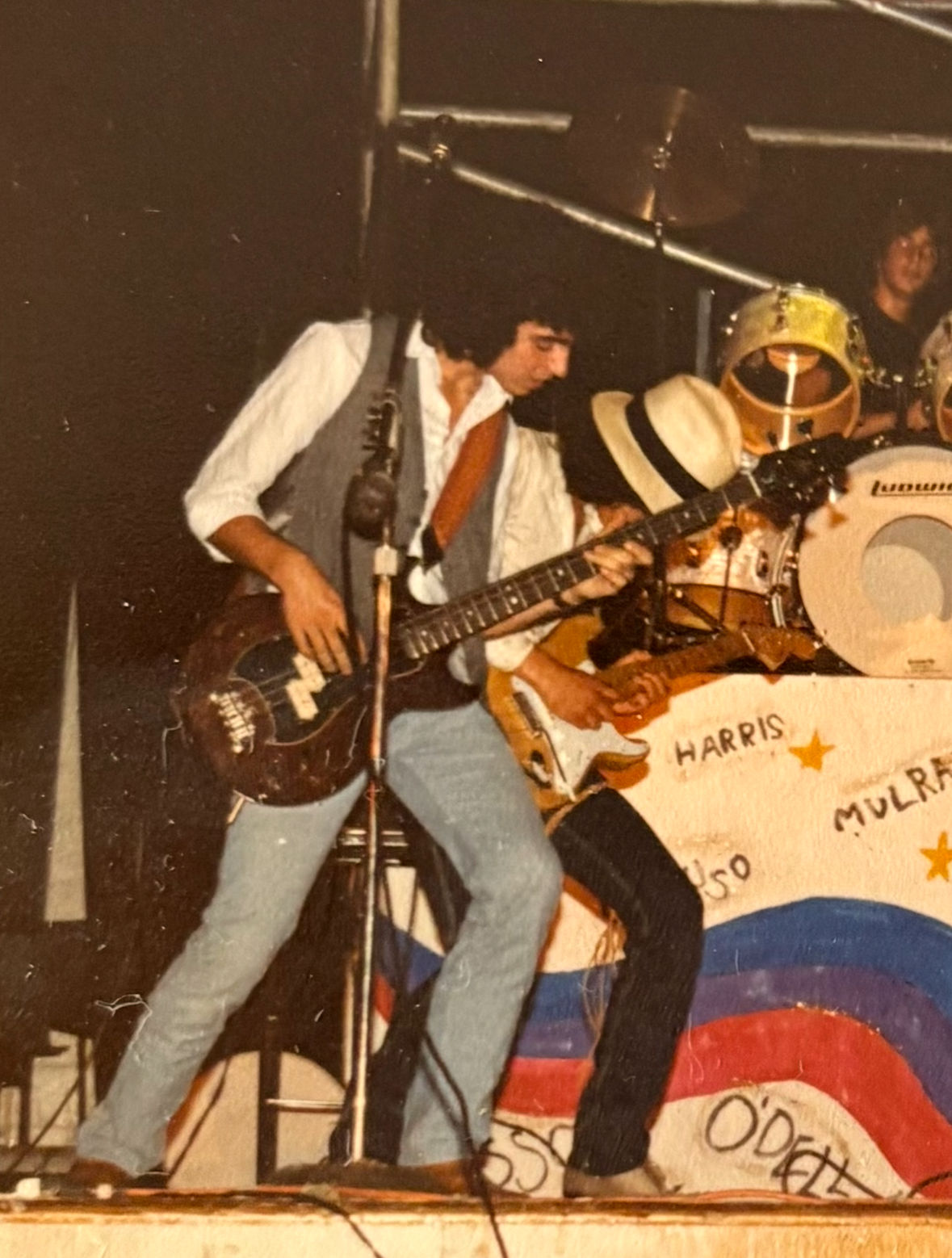 Young Paul O'Dell playing bass on stage, banner reading O'DELL
