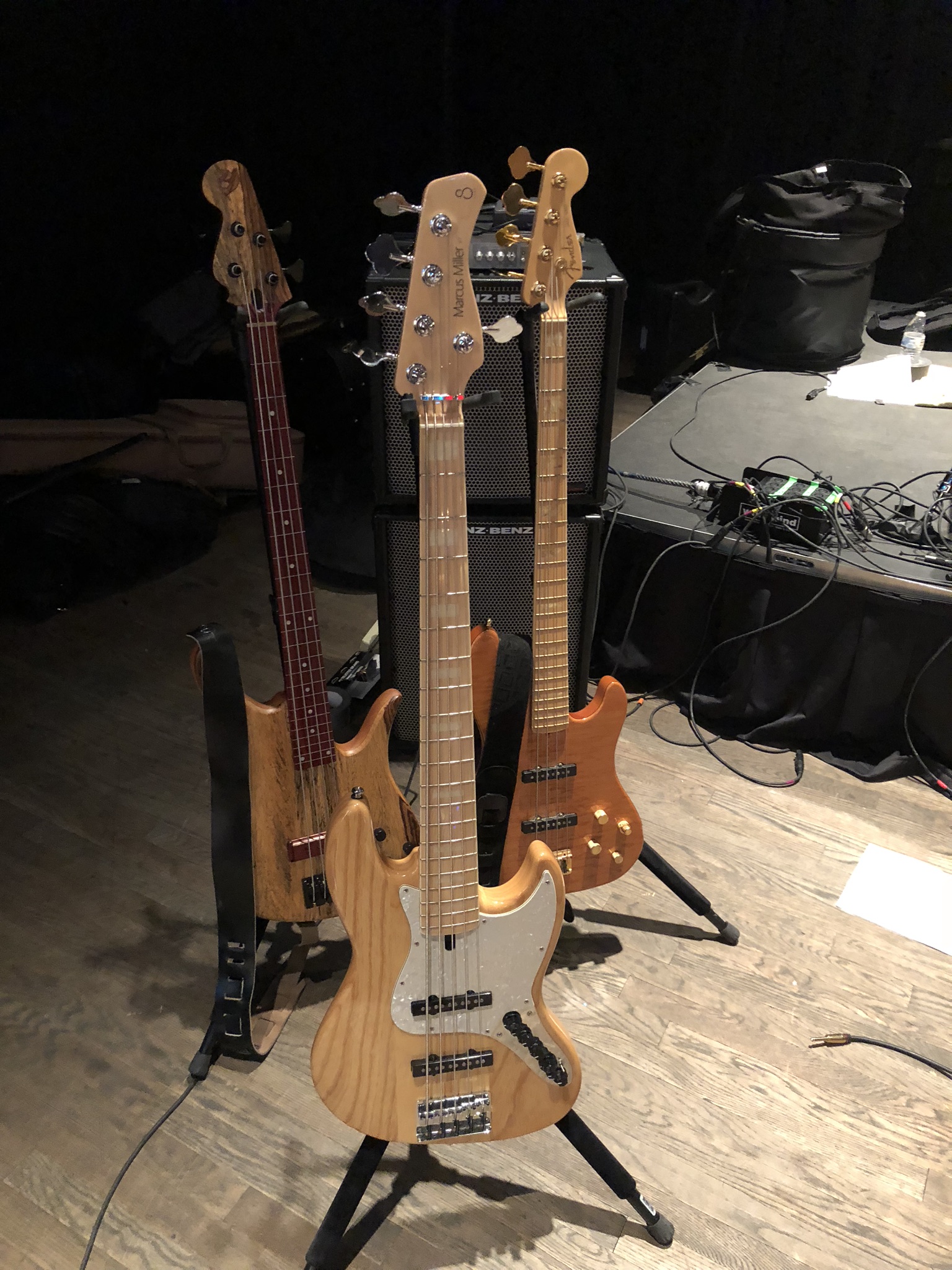 Three bass guitars on stands with Genz-Benz cabinets behind them